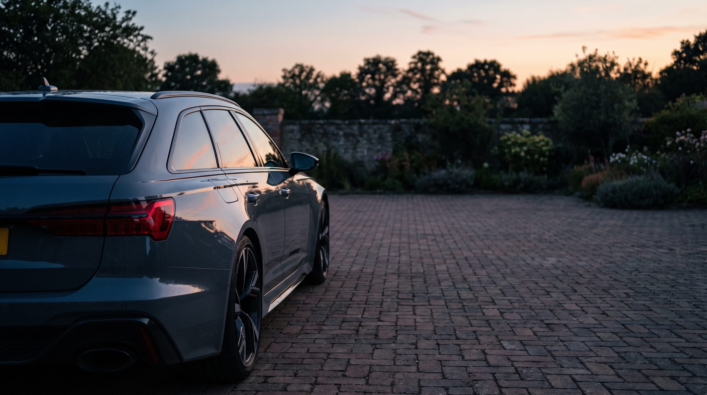 Achterzijde van een Audi RS6 Avant met reflectie van de avondlucht op een oprit