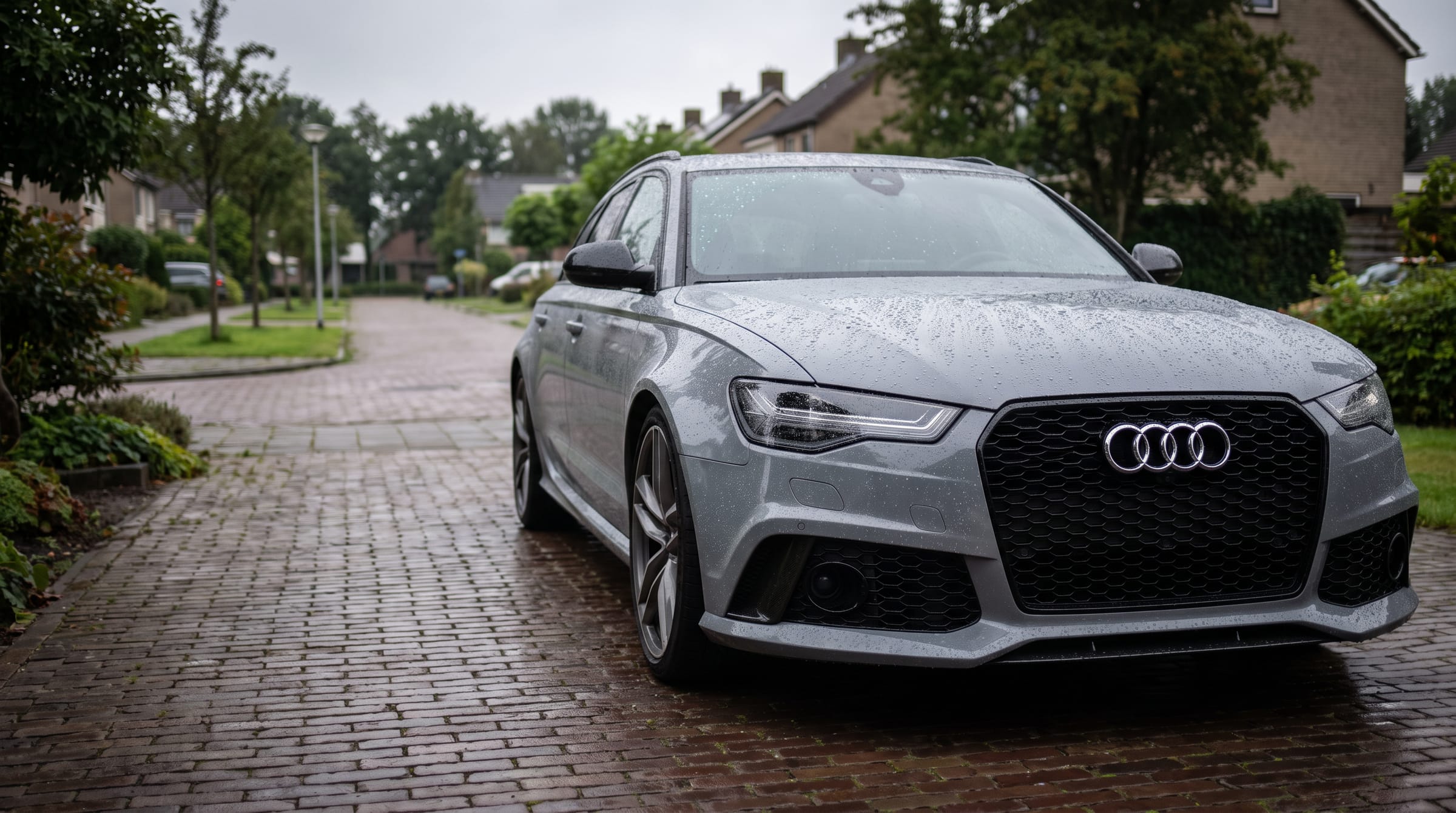 Audi RS6 Avant in Nardo-grijs op een klinker-oprit, net gecoat, met waterdruppels op de motorkap