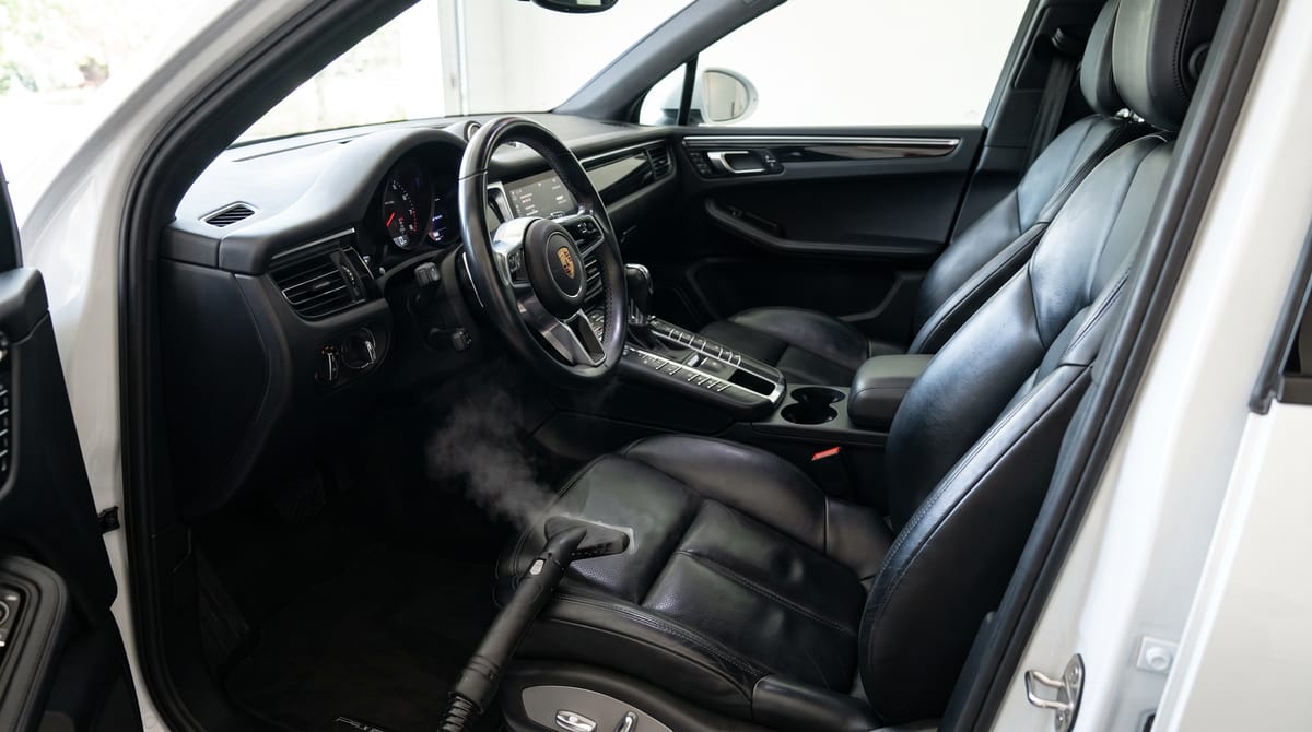 Zwart leren bestuurdersstoel van een Porsche Macan na stoomreiniging, stuur in beeld